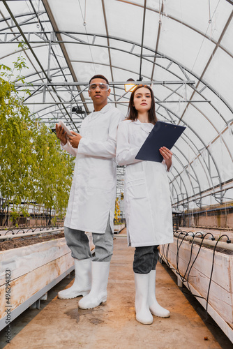 Low angle view of multiethnic botanists holding digital tablet and clipboard in greenhouse. © LIGHTFIELD STUDIOS