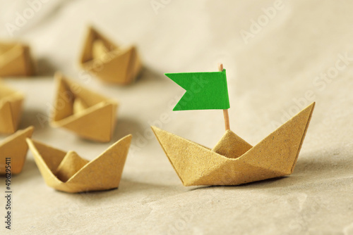 Origami recycled paper boat with green flag leading a group of small boats - Concept of leadership, teamwork and ecology