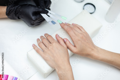 Manicurist selects the color of manicure for the nails of a female client in a nail salon