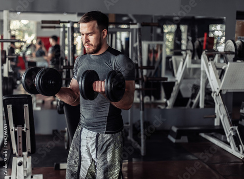 Athletic man training biceps with dumbbells in his hands