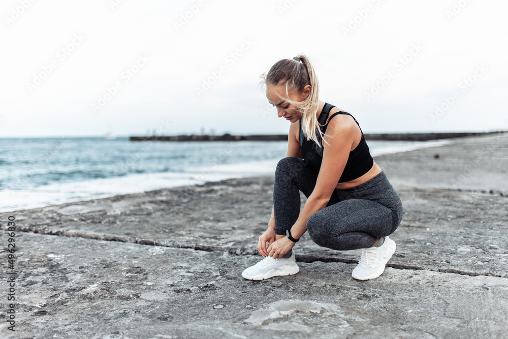 Fit woman tying her shoelaces on urban beach. Healthy lifestyle