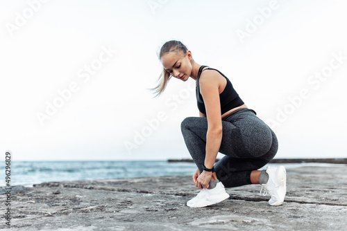 Fit woman tying her shoelaces on urban beach. Healthy lifestyle