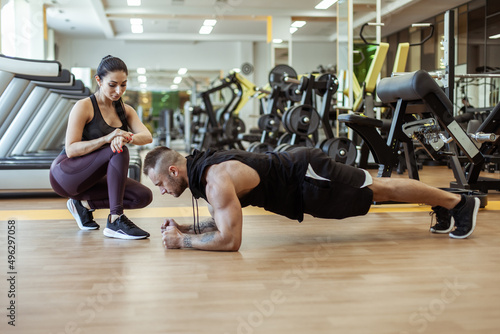 Athletic man doing plank exercise and beautiful girl timed in the gym