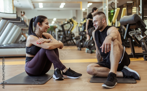 Athletic man and woman talking cute while sitting on mats in the gym. Workout together