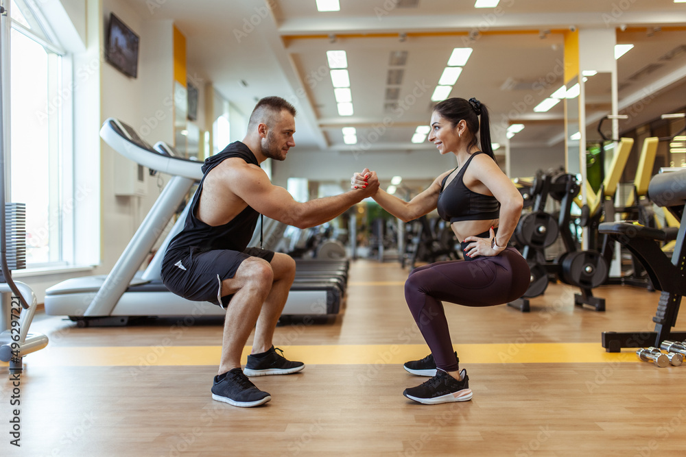 Athletic man with woman squats holding hands in the gym. Workout together .