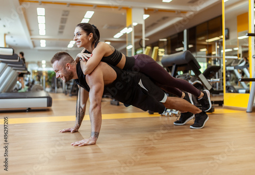 Strong man doing push-ups with a woman on his back in the gym