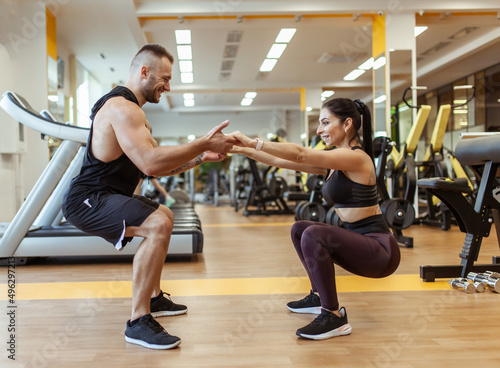 Athletic man with woman squats holding hands in the gym. Workout together .