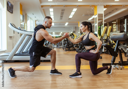 Athletic man with woman doing lunges holding hands in the gym. Workout together