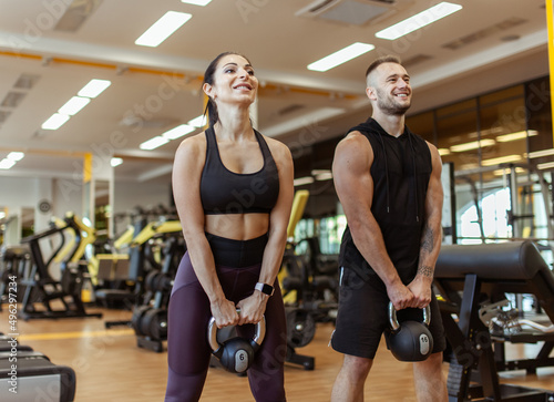 Athletic man and woman training together with kettlebells in modern gym