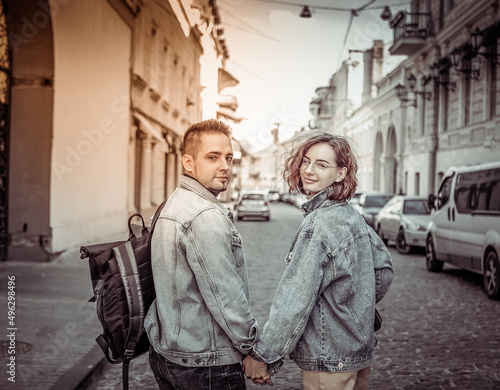 Charismatic modern couple of tourists in love in denim jackets stroll along the urban street