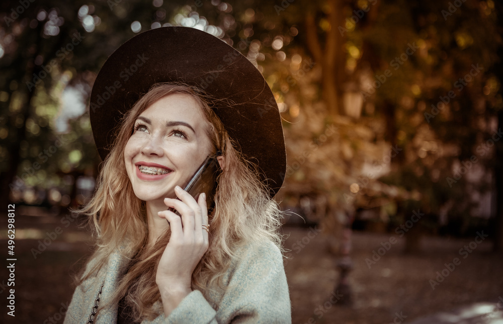 Portrait of a beautiful woman with braces wearing a hat and coat talking on the phone outdoors