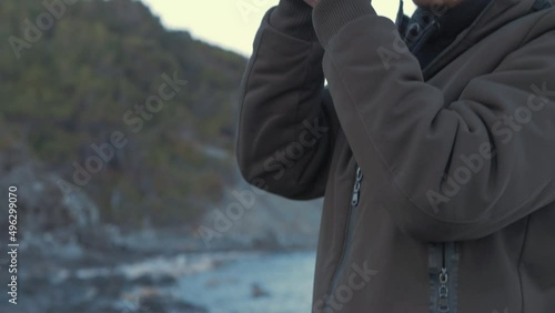 Young man brings camera to eye filming by seaside photo
