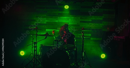 Professional drummer playing on stage during rock show in green spot lights