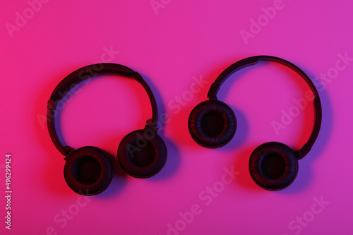 Two pairs of black wireless stereo headphones in pink blue neon light