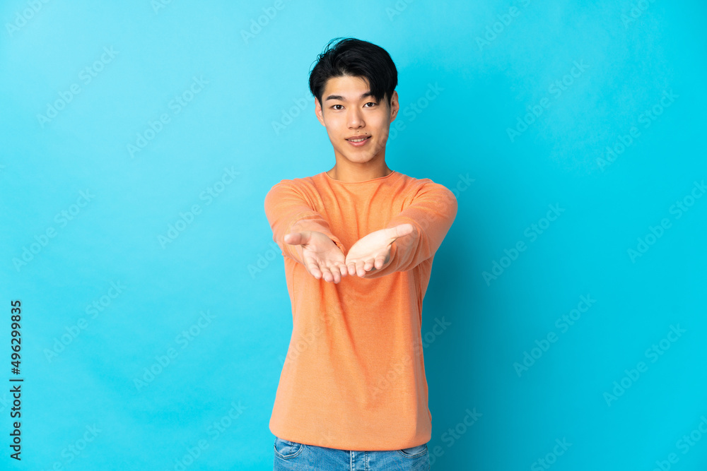 Young Chinese man isolated on blue background holding copyspace imaginary on the palm to insert an ad Young Chinese man isolated on blue background holding copyspace imaginary on the palm to insert an ad