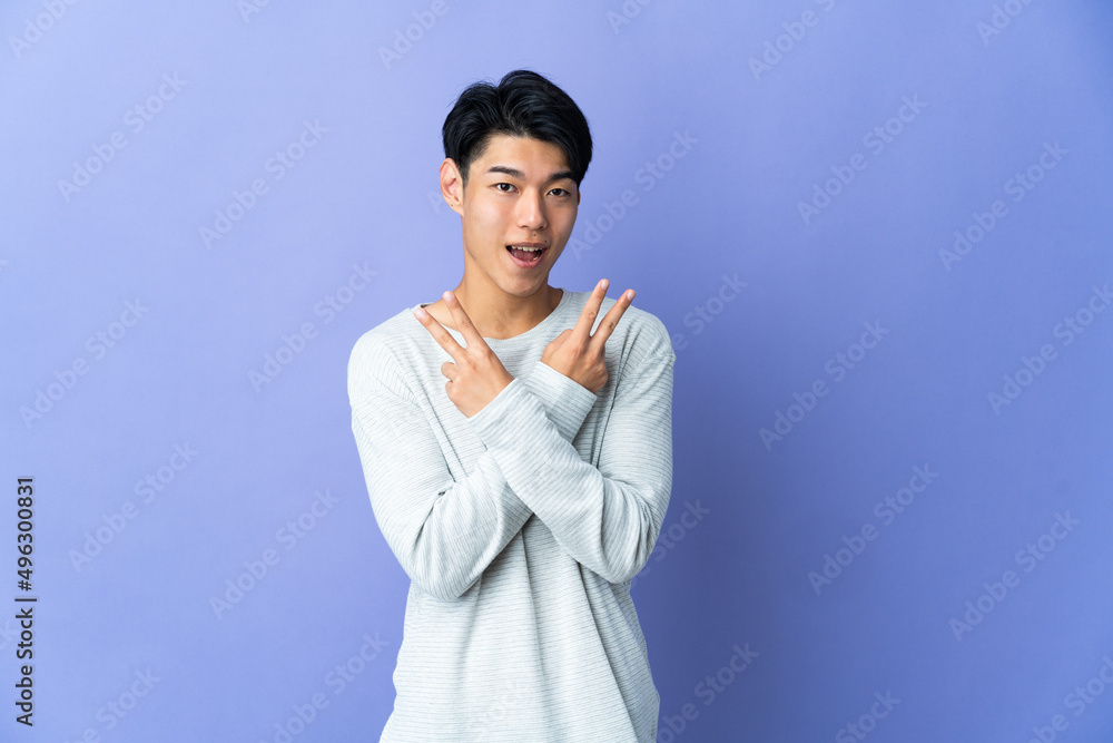 Young Chinese man isolated on purple background smiling and showing victory sign Young Chinese man isolated on purple background smiling and showing victory sign