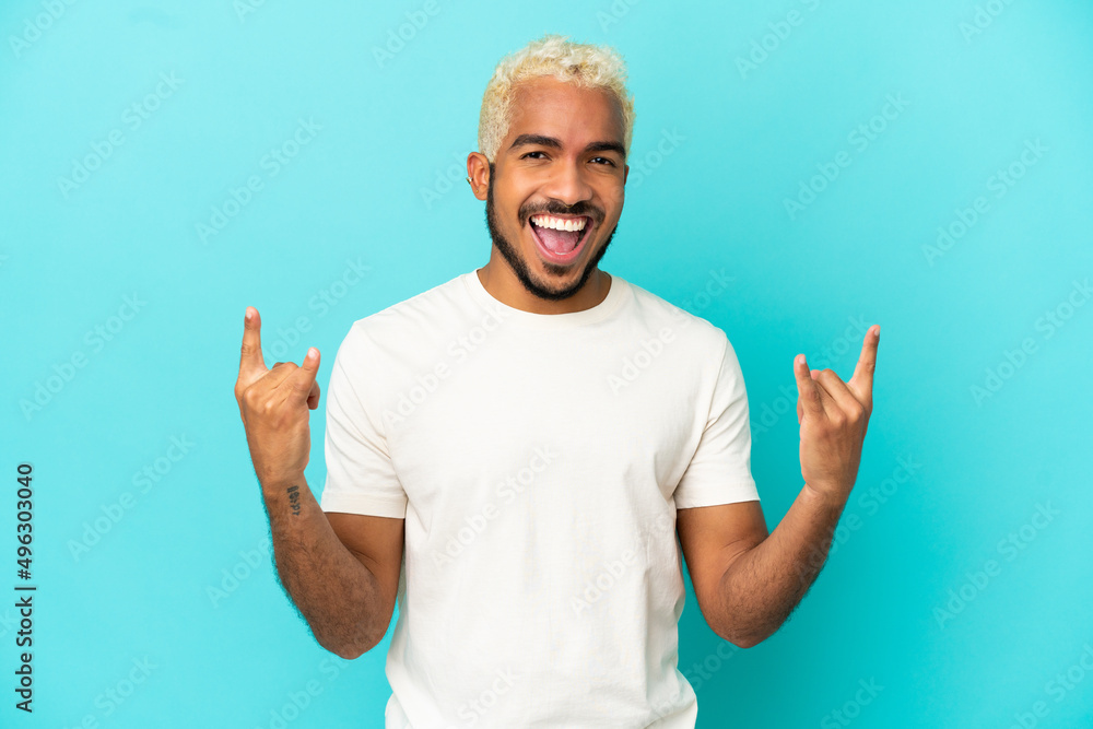 Fototapeta premium Young Colombian handsome man isolated on blue background making horn gesture