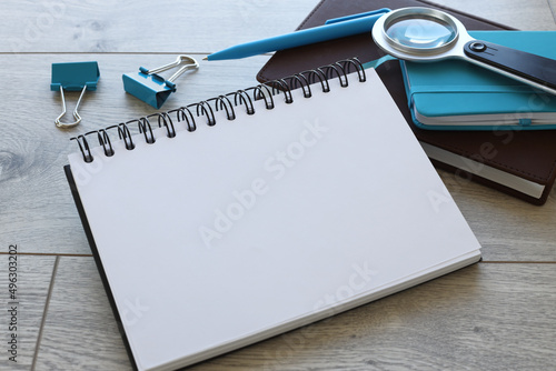 Image of a magnifying glass and a folded spiral notebook lying on a dark brown wooden table near a blue notepad