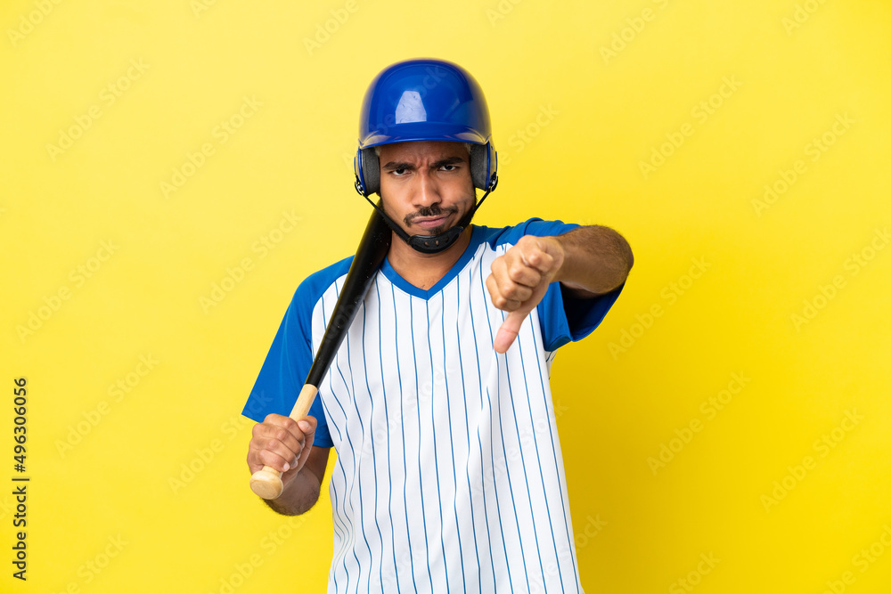 Young Colombian latin man playing baseball isolated on yellow background showing thumb down with negative expression