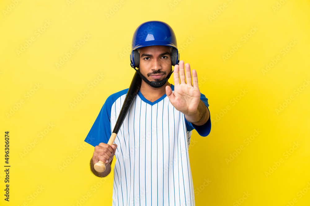 Young Colombian latin man playing baseball isolated on yellow background making stop gesture