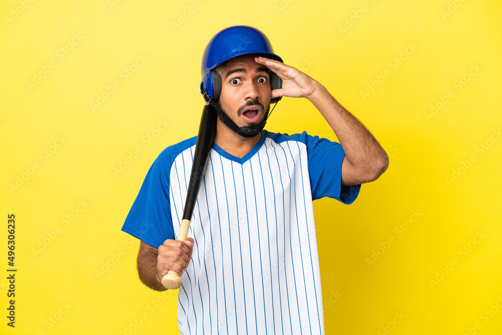 Young Colombian latin man playing baseball isolated on yellow background doing surprise gesture while looking to the side