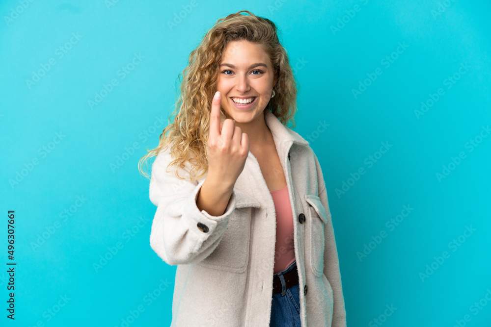 Young blonde woman isolated on blue background doing coming gesture Young blonde woman isolated on blue background doing coming gesture