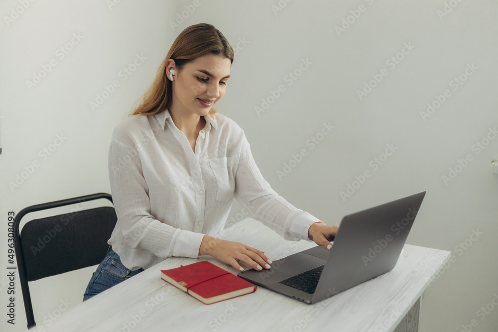 A young beautiful girl in headphones learns with internet chat, a Skype teacher prepares for an exam, a schoolgirl learns online, watches a webinar, takes notes, looks at a laptop, distance learning A young beautiful girl in headphones learns with internet chat, a Skype teacher prepares for an exam, a schoolgirl learns online, watches a webinar, takes notes, looks at a laptop, distance learning