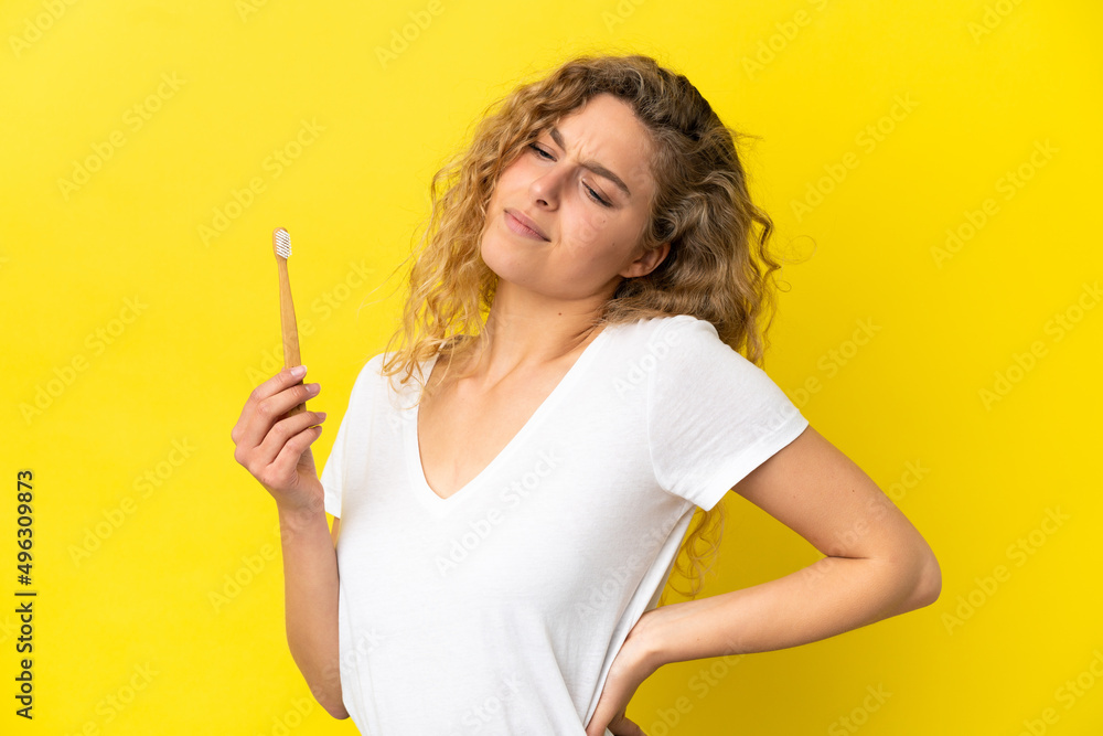 Young caucasian woman holding a brushing teeth isolated on yellow background suffering from backache for having made an effort Young caucasian woman holding a brushing teeth isolated on yellow background suffering from backache for having made an effort