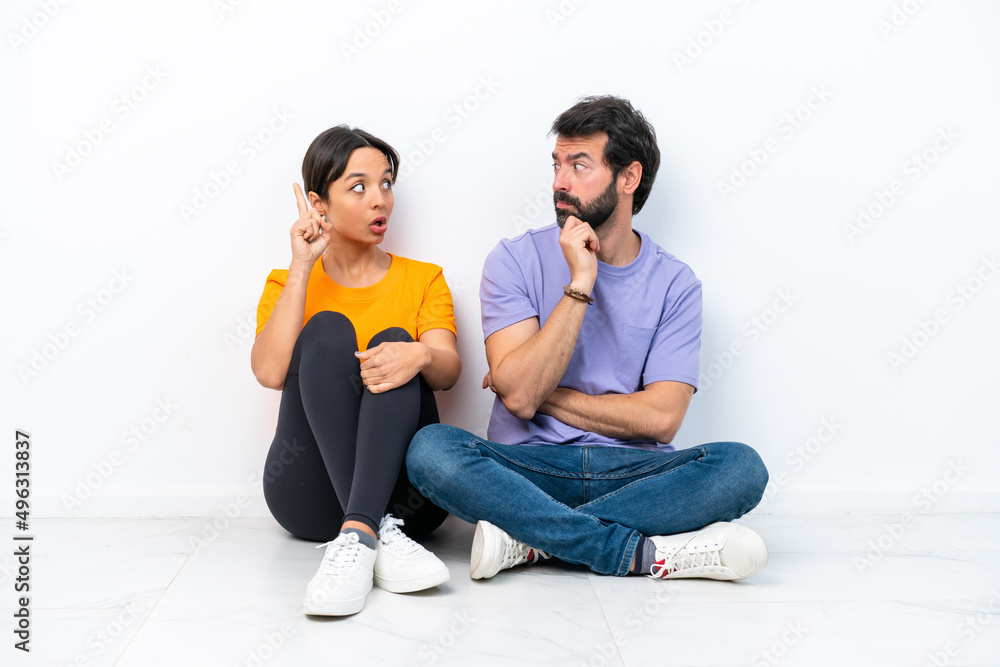Young caucasian couple sitting on the floor isolated on white background standing and thinking an idea Young caucasian couple sitting on the floor isolated on white background standing and thinking an idea