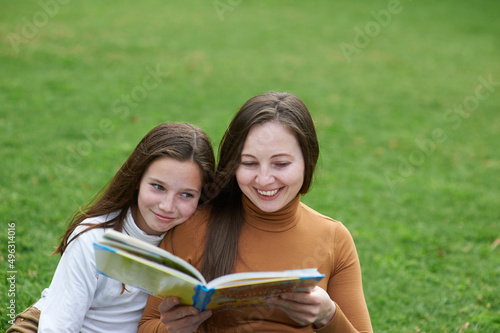 mother and daughter reading a book together in a green park