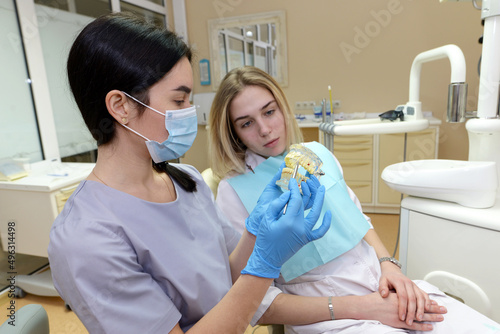 A female dentist shows an artificial jaw to a patient