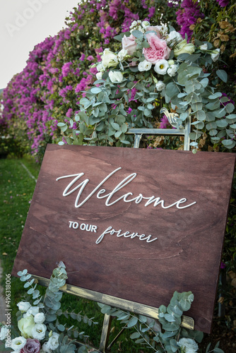 Cartello in legno con su scritto "Welcome"nero contesto di un giardino con piante e fiori 