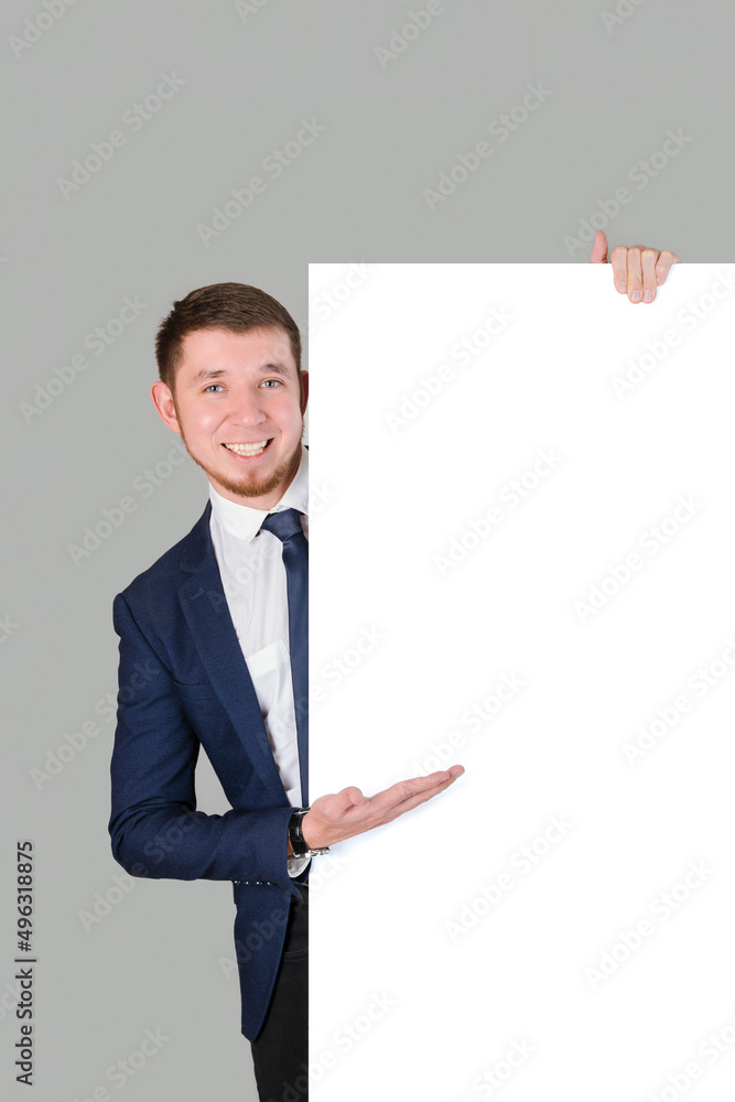 The businessman points with his palm at the white blank board, standing on a gray background