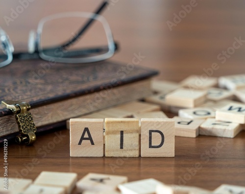 aid word or concept represented by wooden letter tiles on a wooden table with glasses and a book photo