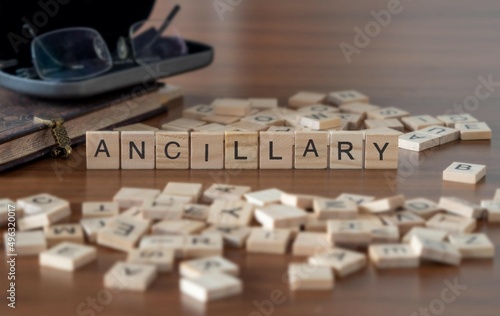 ancillary word or concept represented by wooden letter tiles on a wooden table with glasses and a book