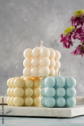 Three bubble candles - off-white, beige-colored and blue - on marble board on pale blue surface