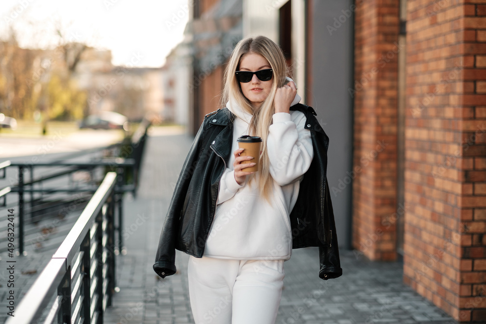 Drinking coffee and having rest. Walking on the city street wearing white sweatshirt.
