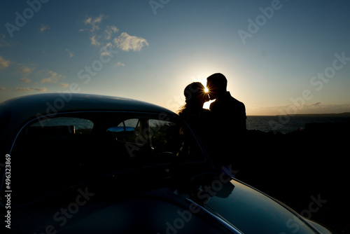 coppia di sposi che si abbracciano in silhouette al tramonto vicino a un auto d'epoca