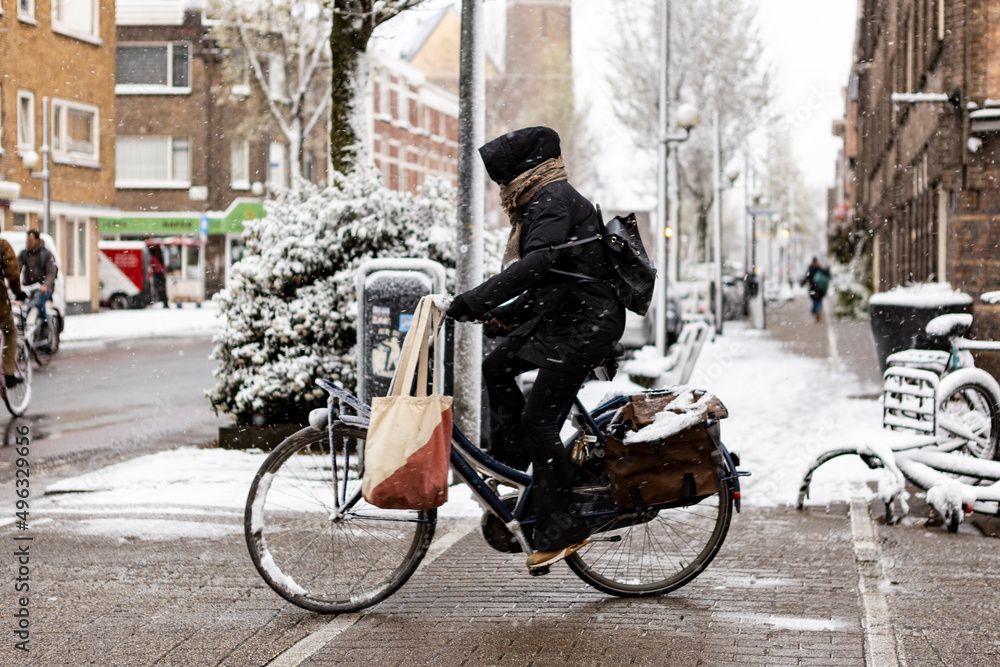 Biker warmly dressed on Dutch bicycle riding through street of Utrecht Lombok neighbourhood covered in snow 
