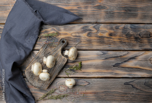 Raw mushrooms on a wooden plank. Dried rosemary is scattered on the table. Dark wooden background, space for text