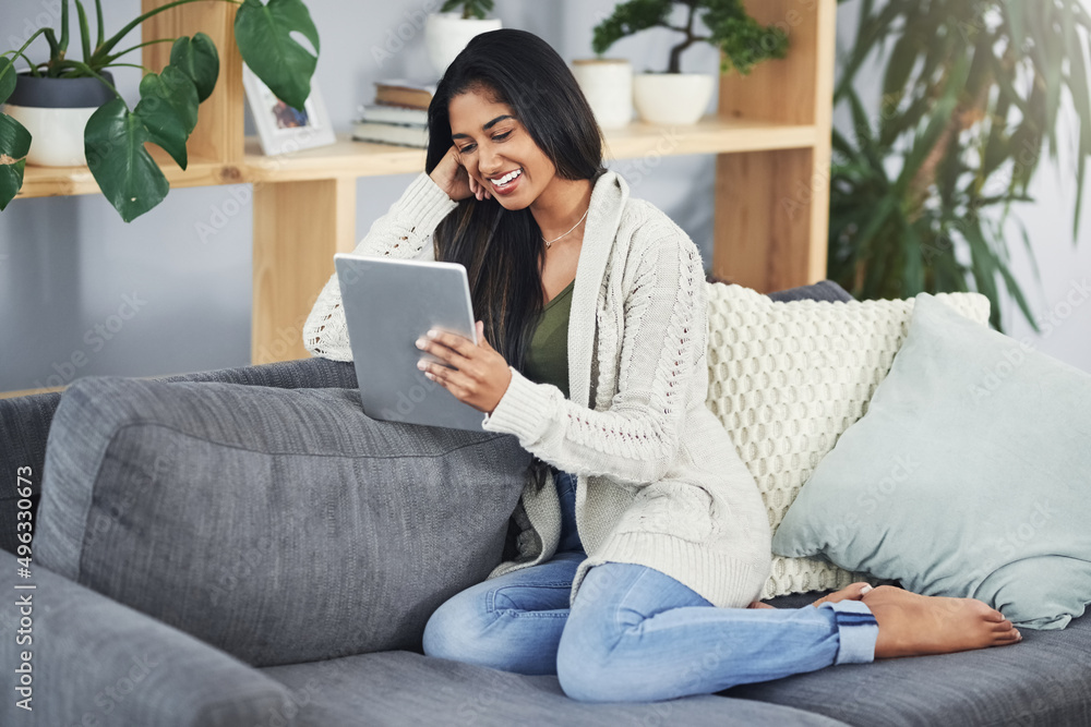 These modern-day sites can sure make ones day. Shot of a happy young woman using her digital tablet while relaxing on her couch at home. These modern-day sites can sure make ones day. Shot of a happy young woman using her digital tablet while relaxing on her couch at home.