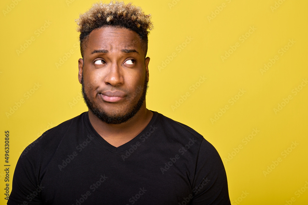 A dark-skinned man with a beard with a smirk on his face looks to the side in disapproval, faced with a difficult choice, dressed in an everyday black T-shirt. Doubting guy looks up with a smirk A dark-skinned man with a beard with a smirk on his face looks to the side in disapproval, faced with a difficult choice, dressed in an everyday black T-shirt. Doubting guy looks up with a smirk