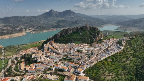 Flying over the orange roofs of the town, fortress on the mountain and the view of the river in Zahara de la sierra.