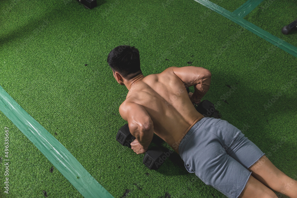 A fit guy with a shredded physique does a set of dumbbell pushups at