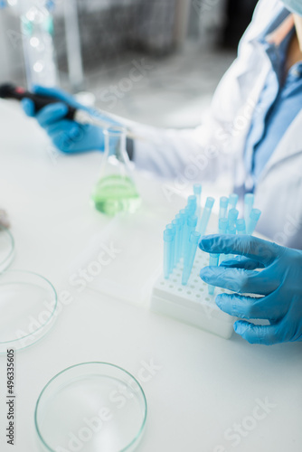 cropped view of blurred geneticist in latex gloves near test tubes.