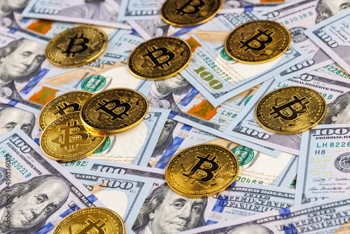 yellow bitcoin coins scattered over US dollar paper banknotes, closeup with selective focus photo