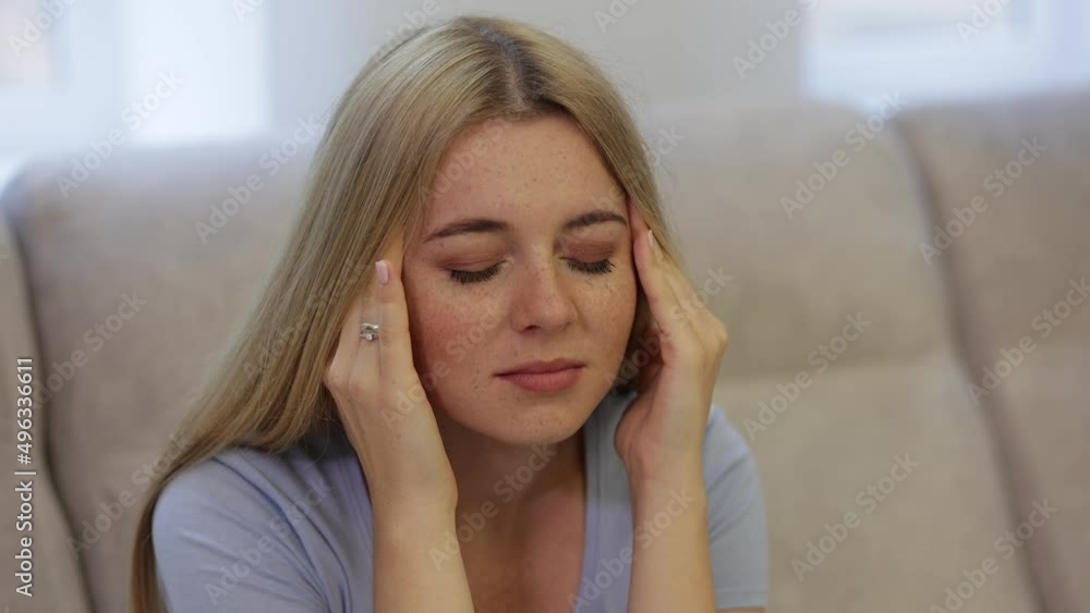 a woman suffering from a headache sits on a sofa, holding her hands near her eyelids and makes massage movements. a woman suffering from a headache sits on a sofa, holding her hands near her eyelids and makes massage movements.