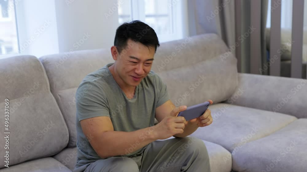 a man sits on a sofa, holds a phone joyful from the news, dances, makes a win gesture. a man sits on a sofa, holds a phone joyful from the news, dances, makes a win gesture.