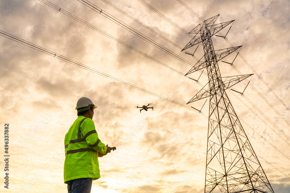 Engineer location use drone to fly inspections at the electric power station to view the planning work by producing electricity high voltage electric transmission tower at sunset. Engineer location use drone to fly inspections at the electric power station to view the planning work by producing electricity high voltage electric transmission tower at sunset.