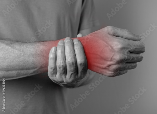 Man suffering from wrist pain and holding painful hand with red point. Inflammation of tissues, tendons. Carpal tunnel syndrome. Physical overload. High quality photo